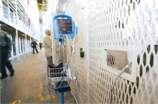 A prisoner patient waits in a cage outside the East Block Death Row clinic, having his vital signs taken through the door port before seeing his attending physician.