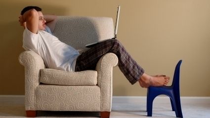Man sitting on a club chair reading from his laptop.