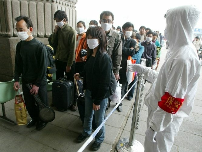 A railway worker wearing protective clothing to ward off the SARS virus controls a line of travelers as they wait to enter Beijing's West Railway Station Tuesday in 2003.