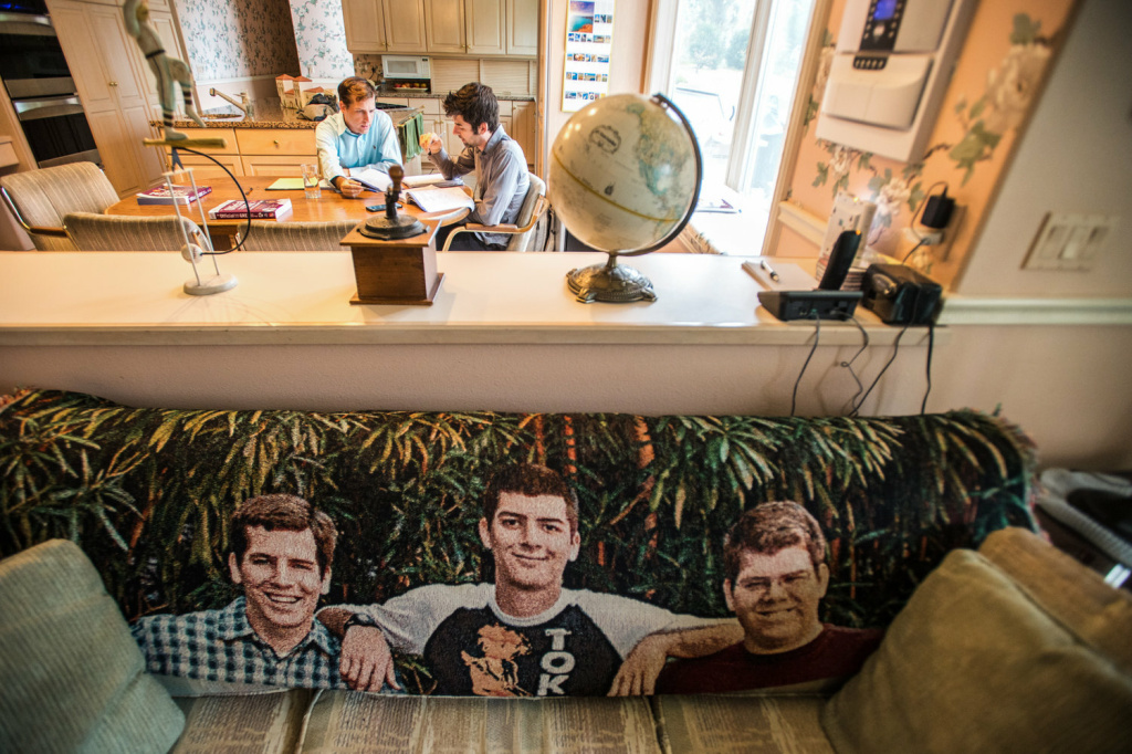 Charles (right) gets tutoring from his brother David on the GRE test at their parents' home. The couch in the living room bears a blanket with images of the three Mayer brothers.