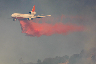 A 10 Tanker, DC-10 firefighting jet, flies through a smoky sky while dropping Phos-Check fire retardant as firefighters try to prevent the 3,500-acre Sheep fire from reaching the mountain town of Wrightwood, a half-mile away, on October 4, 2009 near Wrightwood, California.