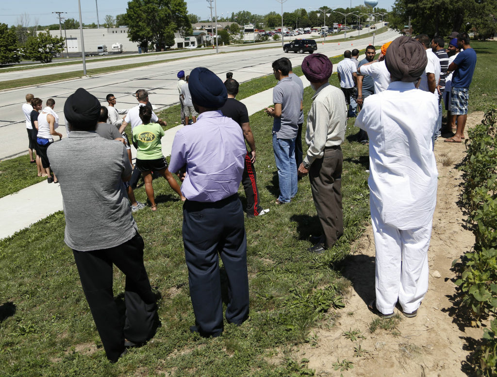 Bystanders look on as SWAT officers surround the Sikh Temple of Wisconsin where at least one gunman stormed a mass and opened fire August, 5, 2012 Oak Creek, Wisconsin. At least six people were killed when a shooter, who was shot dead by a police officer, opened fire on congregants in the Milwaukee suburb.