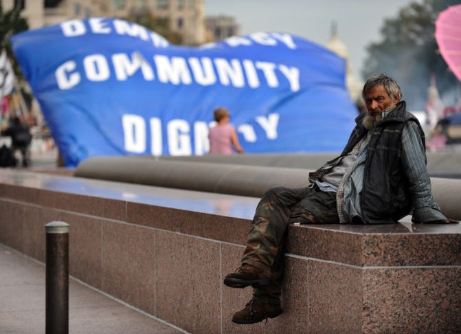 A homeless man sits near a banner during