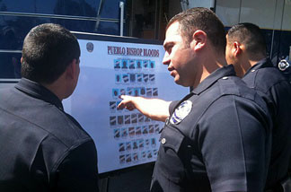 LAPD officer Manuel Gomez and others look at poster of Pueblo Bishops Bloods after a sweep operation.