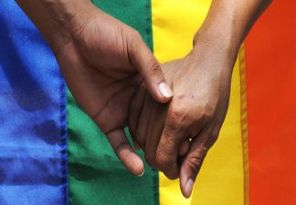 Two hands embrace in front of a rainbow flag. File photo.