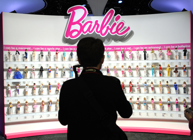 A woman photographs a wall of Barbie dolls