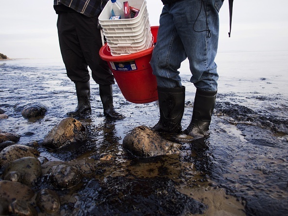 Local residents stand on oil covered rocks and sand at Refugio State Beach in Goleta, California, May 19, 2015.
