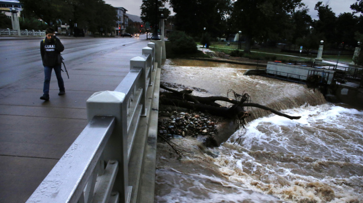A woman walks past Boulder Creek, whose swollen waters have receded a bit after intense rain that fell for days has abated, in Boulder, Colo., Sunday.