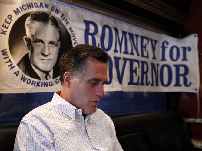 Mitt Romney reads on his campaign bus earlier this year. A 1960s campaign poster supporting his father, George, is behind him.