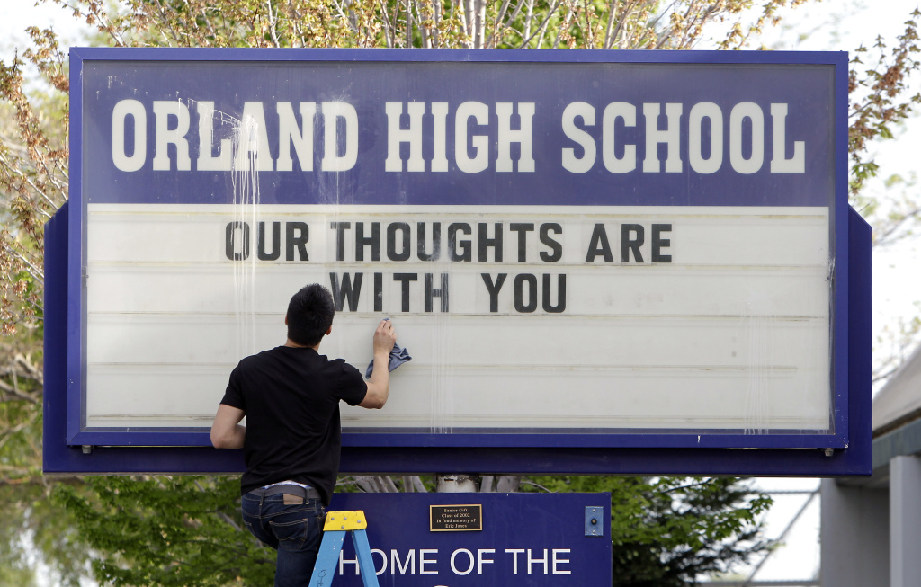 Sergio Parra, 16, a 10th grader at Orland High School, cleans the glass on the school's sign, Friday, April 11, 2014, after placing a memorial remembering the victims of a fiery crash between a tour bus and a FedEx truck in Orland, Calif.