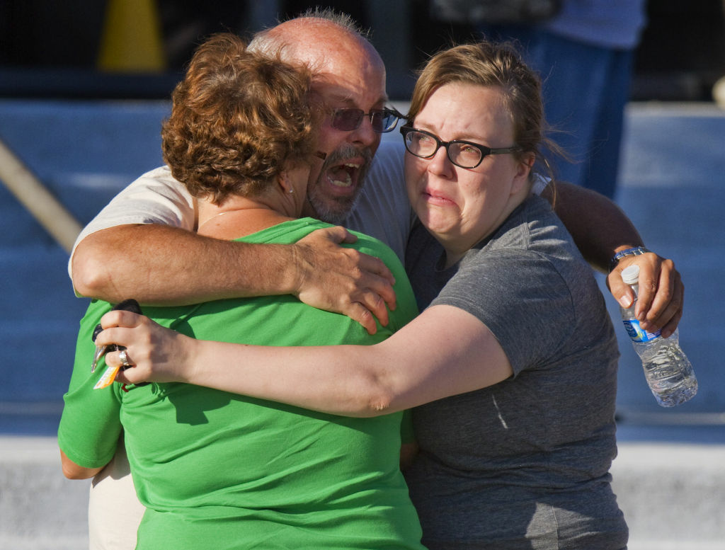 Tom Sullivan, center, embraces family members outside Gateway High School where he has been searching frantically for his son Alex Sullivan who celebrated his 27th birthday by going to see "The Dark Knight Rises."