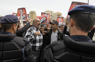 Lebanese riot policemen stand guard as Syrian protesters carry pictures of Syrian President Bashar Assad as they shout pro-government slogans in front of the U.N. house in downtown Beirut, Lebanon, Monday, May 2, 2011.