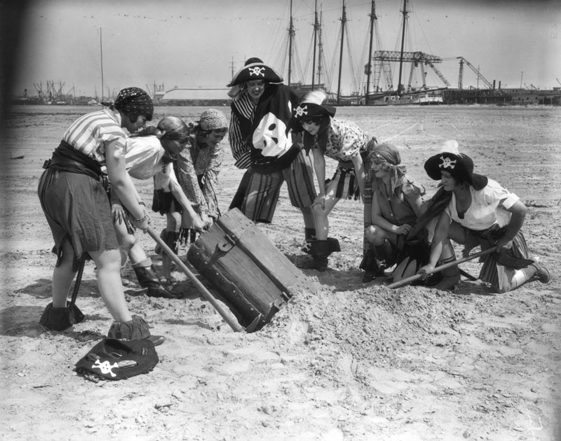 Women pirates in costume pull a buried treasure chest from a hole they dug on the beach at the 1928 Pacific Southwest Exposition in Long Beach.