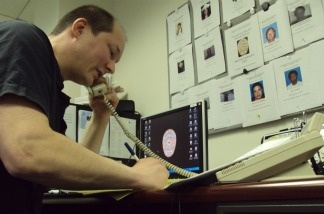Actor and volunteer detective James Elliott makes calls in front of a board with pictures of missing people.