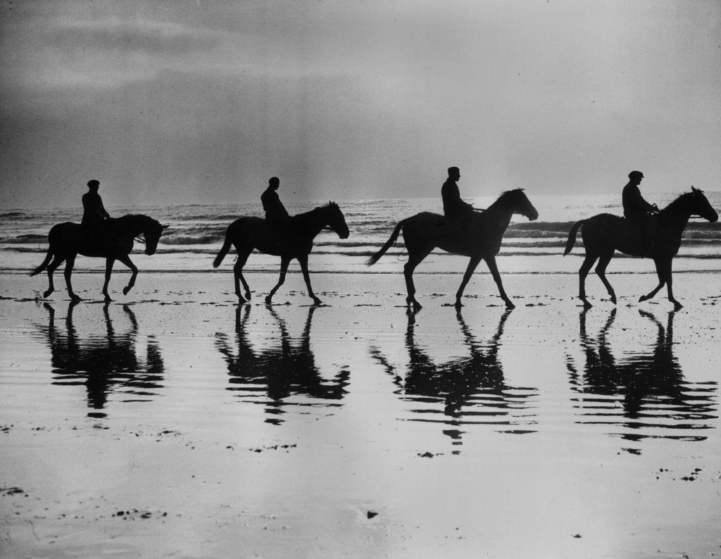14th February 1938: Racehorses being trained by David Dale are silhouetted against the skyline as they walk along the beach at Newhaven, Sussex. David Dale believes in sea water to strengthen their legs. Left to right; Ontario II, Tabrian II, Serpentare and Irish Challenge. (Photo by Reg Speller/Fox Photos/Getty Images)