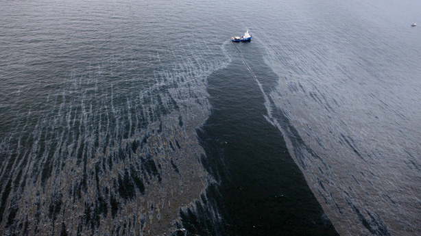 A boat with an oil boom tries to contain the spill, approximately seven miles from where the oil rig sunk last week.