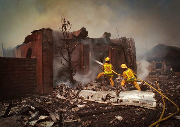 Firefighters battle flames from a burning home in Cerritos, Calif., in this Aug. 31, 1986 file photo, as they straddle pieces of fuselage from an AeroMexico jetliner.