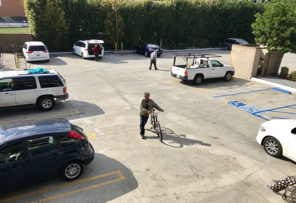 OC riverbed homeless Fritz Reichenbach pushes his bicycle across the parking lot of the Buena Park motel he's staying at.