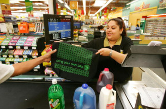 Mercer 8201 Food 4 Less grocery store general clerk Xochil Montenegro hands out a free reusable shopping bag, supplied by the California Grocers Association (CGA) and the City of Los Angeles, to a customer in observance of Earth Day, on the eve of Earth Day, April 21, 2008 in Los Angeles, California. During the two-day program, 50,000 bags are being handed out at about 40 grocery stores to encourage consumers to use reusable bags instead of disposable plastic or paper bags. The use of reusable bag has increased since a statewide plastic bag recycling law was enacted in July 2007 requiring grocers to provide in-store plastic bag recycling and to sell reusable shopping bags. Some communities have banned disposable plastic grocery bags. The free bags provided by the CGA and the city are made of 100% recycled water, soda and food containers.