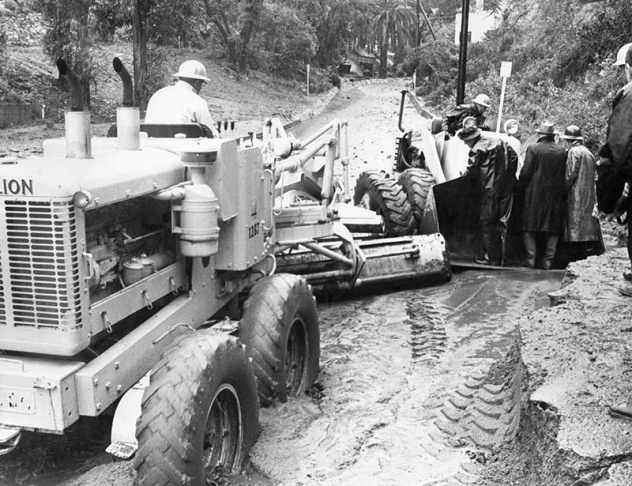1938: People walk along the flooded L.A. River near the Dayton Avenue Bridge. In the background, a railroad bridge hangs in a twisted heap after one of the pilings has collapsed. (Photograph courtesy of the Los Angeles Public Library)