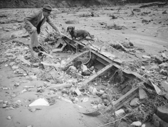 1938: People walk along the flooded L.A. River near the Dayton Avenue Bridge. In the background, a railroad bridge hangs in a twisted heap after one of the pilings has collapsed. (Photograph courtesy of the Los Angeles Public Library)