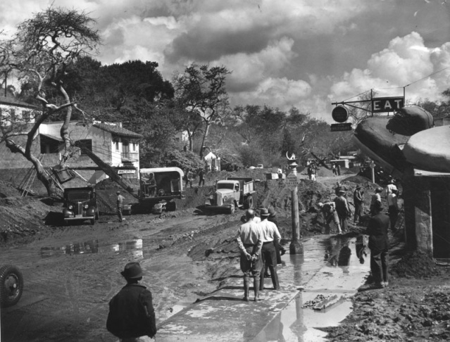 1938: People walk along the flooded L.A. River near the Dayton Avenue Bridge. In the background, a railroad bridge hangs in a twisted heap after one of the pilings has collapsed. (Photograph courtesy of the Los Angeles Public Library)