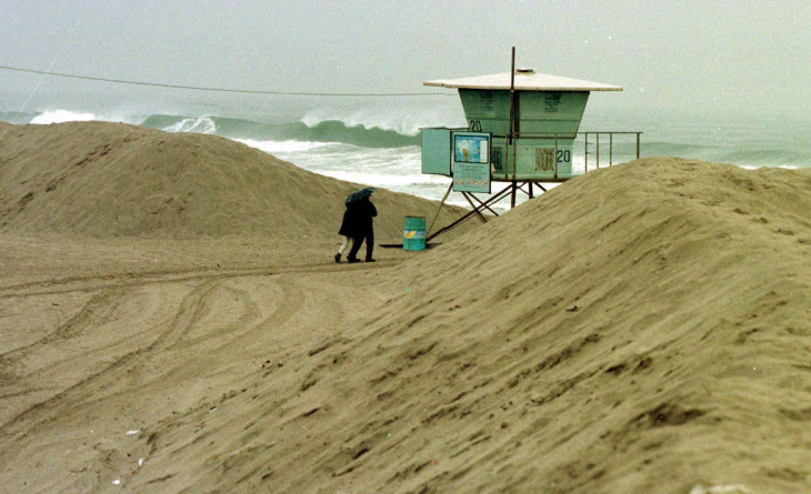 1938: People walk along the flooded L.A. River near the Dayton Avenue Bridge. In the background, a railroad bridge hangs in a twisted heap after one of the pilings has collapsed. (Photograph courtesy of the Los Angeles Public Library)