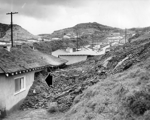 1938: People walk along the flooded L.A. River near the Dayton Avenue Bridge. In the background, a railroad bridge hangs in a twisted heap after one of the pilings has collapsed. (Photograph courtesy of the Los Angeles Public Library)