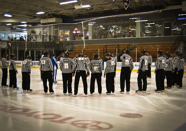 National Hockey League referees gather students in a huddle to teach them how to be better hockey officials.