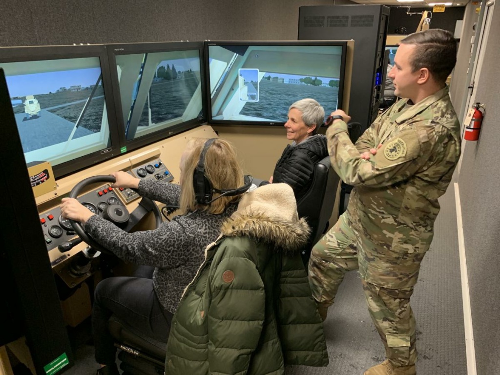American Homefront Teachers 2 Teachers Kate Bridgman (left) and Lisa Jolstad of Cheyenne Mountain High School in Colorado, sit in a driving simulator at Fort Carson while Army Capt. Wes Barber looks on.