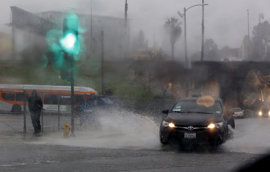 File: Raindrops bead upon a windshield as a pedestrian walks through rain in downtown Los Angeles, Friday, Jan. 20, 2017.
