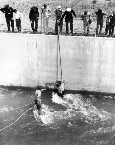 1938: People walk along the flooded L.A. River near the Dayton Avenue Bridge. In the background, a railroad bridge hangs in a twisted heap after one of the pilings has collapsed. (Photograph courtesy of the Los Angeles Public Library)