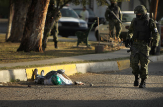 A member of the military police walks by a body with a mask in the street, one of numerous murders over a 24 hour period, on March 26, 2010 in Juarez, Mexico. The border city of Juarez, Mexico has been racked by violent drug related crime recently and has quickly become one of the most dangerous cities in the world to live.