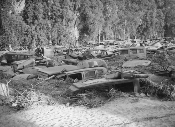 1938: People walk along the flooded L.A. River near the Dayton Avenue Bridge. In the background, a railroad bridge hangs in a twisted heap after one of the pilings has collapsed. (Photograph courtesy of the Los Angeles Public Library)
