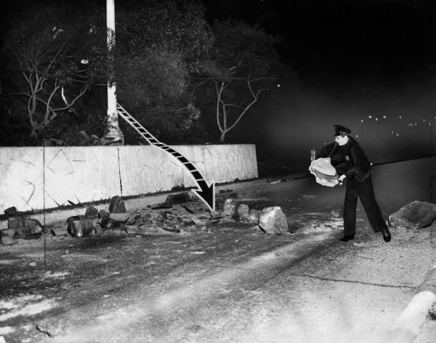 1938: People walk along the flooded L.A. River near the Dayton Avenue Bridge. In the background, a railroad bridge hangs in a twisted heap after one of the pilings has collapsed. (Photograph courtesy of the Los Angeles Public Library)