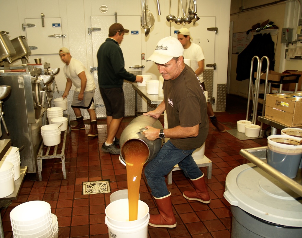 Chris Fosselman Chris Fosselman, forefront, pours salted caramel into a bucket to use in a mixer. John, center back, coordinates the hand packing with other staff members.