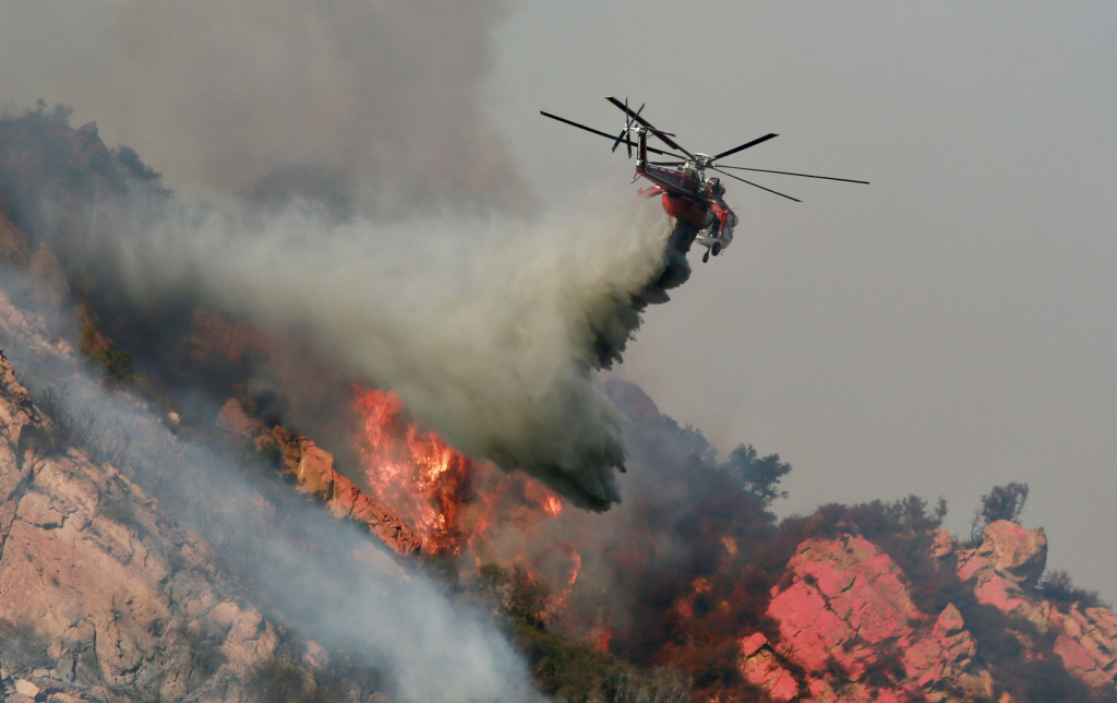 A helicopter drops flame retardant on a wildfire on November 10, 2018 in Malibu, California. The Woolsey fire has burned over 70,000 acres and has reached the Pacific Coast at Malibu as it continues grow. MALIBU, CA - NOVEMBER 11: A helicopter drops flame retardant on a wildfire on November 10, 2018 in Malibu, California. The Woolsey fire has burned over 70,000 acres and has reached the Pacific Coast at Malibu as it continues grow. (Photo by Sandy Huffaker/Getty Images)