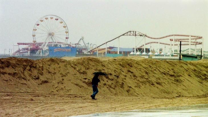 1938: People walk along the flooded L.A. River near the Dayton Avenue Bridge. In the background, a railroad bridge hangs in a twisted heap after one of the pilings has collapsed. (Photograph courtesy of the Los Angeles Public Library)