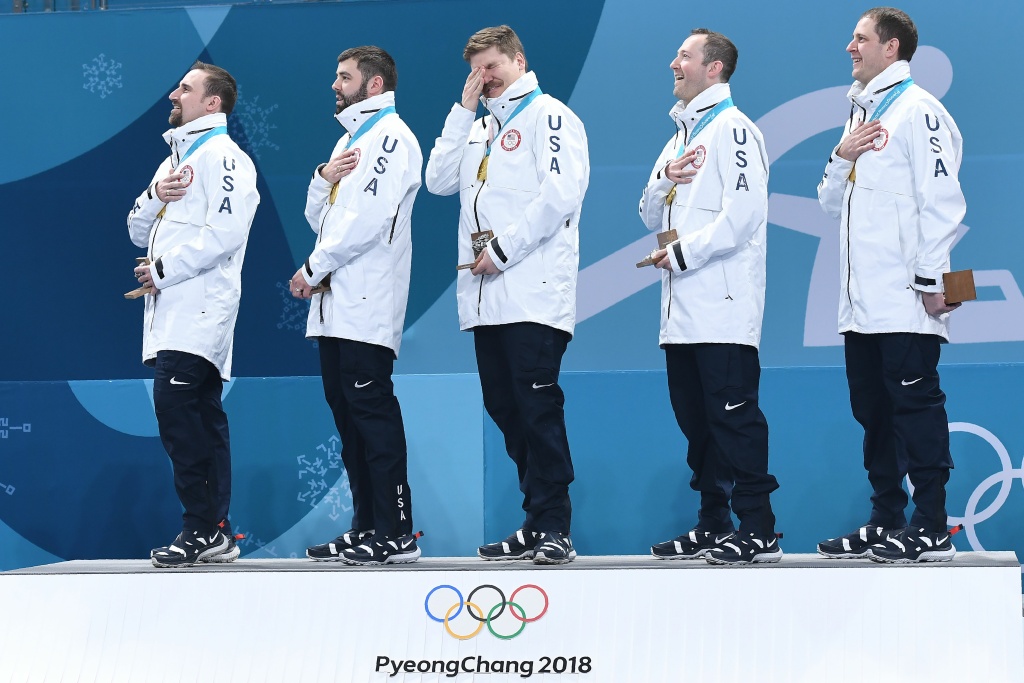 TOPSHOT-CURLING-OLY-2018-PYEONGCHANG-USA-SWE-PODIUM TOPSHOT - USA's Matt Hamilton (C) reacts as his team listens to their national anthem after winning curling men's gold medal game between the USA and Sweden during the Pyeongchang 2018 Winter Olympic Games at the Gangneung Curling Centre in Gangneung on February 24, 2018. / AFP PHOTO / WANG Zhao (Photo credit should read WANG ZHAO/AFP/Getty Images)