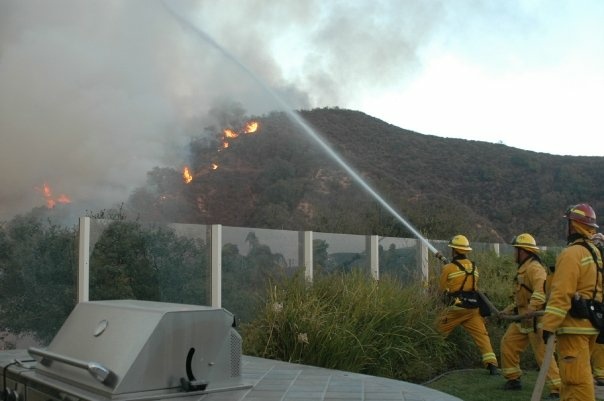 Firefighters battle the flames of the 2007 Santiago Fire in Orange County from the backyard of a home. File photo.