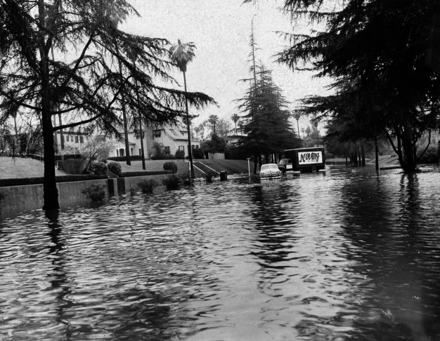 1938: People walk along the flooded L.A. River near the Dayton Avenue Bridge. In the background, a railroad bridge hangs in a twisted heap after one of the pilings has collapsed. (Photograph courtesy of the Los Angeles Public Library)