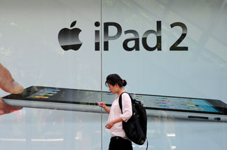 File photo: A woman checks her cell phone while walking past advertising for the ipad 2 in Beijing on June 3, 2011.