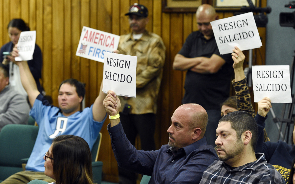 Anti Military Teacher Pico Rivera, Calif. City Council meeting attendees hold up signs during a city council meeting at Pico Rivera City Hall on Tuesday, Feb. 13, 2018, in Pico Rivera, Calif. The city council passed a resolution Tuesday asking for the resignation of city councilman and El Rancho High School teacher Gregory Salcido, who was recorded making anti-military remarks to his students in January.