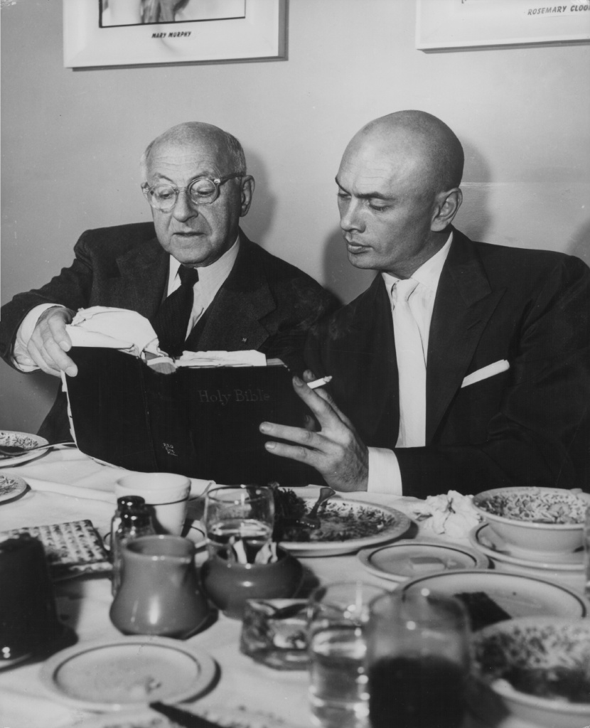 Cecil B DeMille And Yul Brynner Director Cecil B DeMille and actor Yul Brynner discussing a passage from the Holy Bible, prior to the filming of their movie 'The Ten Commandments', circa 1955.