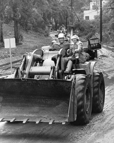 1938: People walk along the flooded L.A. River near the Dayton Avenue Bridge. In the background, a railroad bridge hangs in a twisted heap after one of the pilings has collapsed. (Photograph courtesy of the Los Angeles Public Library)