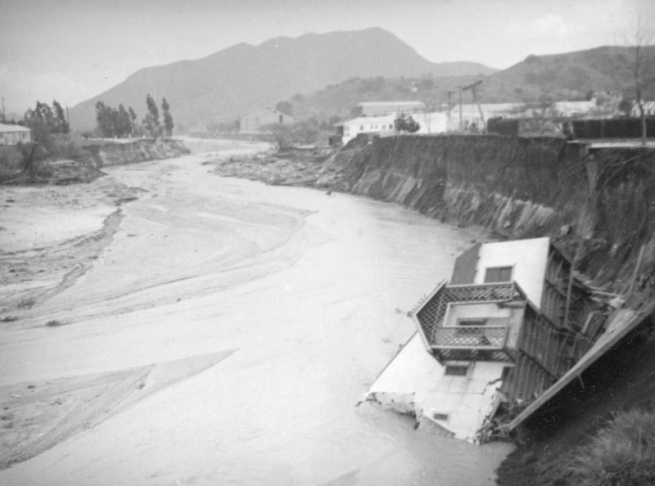 1938: People walk along the flooded L.A. River near the Dayton Avenue Bridge. In the background, a railroad bridge hangs in a twisted heap after one of the pilings has collapsed. (Photograph courtesy of the Los Angeles Public Library)