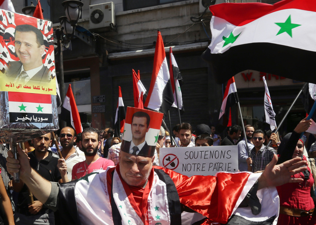 SYRIA-CONFLICT-DEMO A protester, wearing a poster wrapped on his head with the portrait of the Syrian president and draped in a Syrian national flag, takes part in a rally to show support to Syrian President Bashar al-Assad on September 9, 2013 in Damascus.
