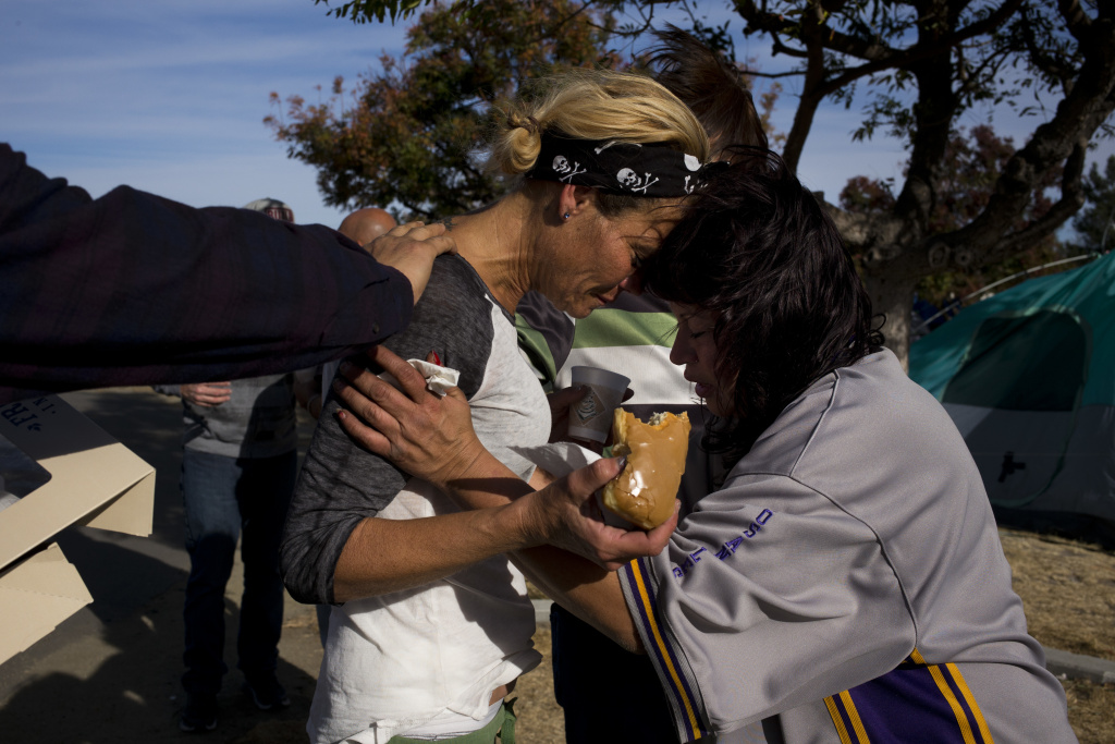 Homeless Crisis Saviors or Enablers Amy Potter, left, and Victoria Pena, who are both homeless, pray for each other while holding donuts and coffee donated by local church members in a homeless encampment on the Santa Ana River trail Saturday, Dec. 9, 2017, in Anaheim, Calif. Goodhearted neighbors heartbroken over the rising number of homeless in their communities are dishing out hot meals, providing mobile showers and handing out sandwiches to those in need.