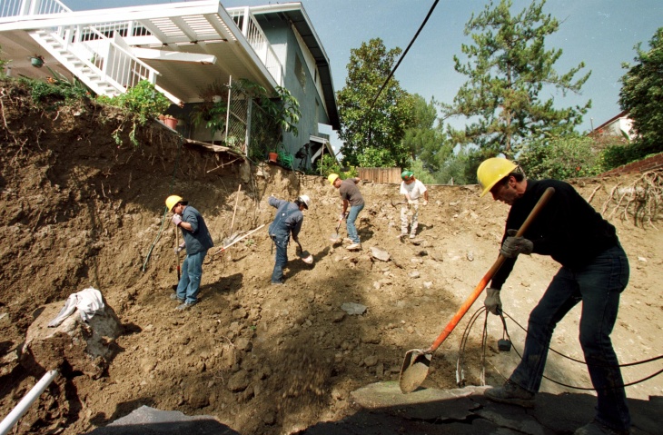 1938: People walk along the flooded L.A. River near the Dayton Avenue Bridge. In the background, a railroad bridge hangs in a twisted heap after one of the pilings has collapsed. (Photograph courtesy of the Los Angeles Public Library)