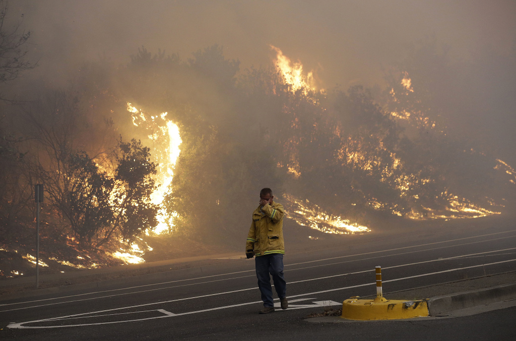 California Wildfires A firefighter covers his eyes as he walks past a burning hillside in Santa Rosa, Calif., Monday, Oct. 9, 2017. Wildfires whipped by powerful winds swept through Northern California, sending residents on a headlong flight to safety through smoke and flames as homes burned.